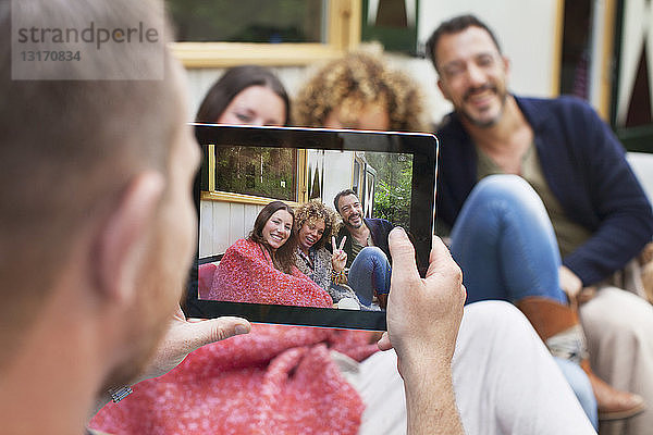 Über-die-Schulter-Ansicht eines Mannes  der Freunde auf einem digitalen Tablet fotografiert