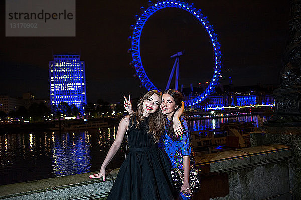 Porträt von zwei Freundinnen  die nachts mit dem London Eye posieren  London  UK