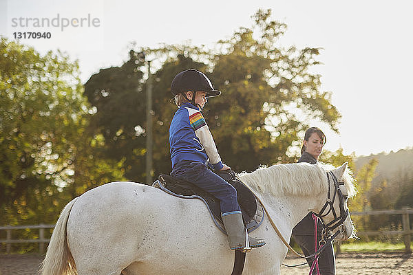 Ausbilder führt Jungen beim Ponyreiten auf dem Reitplatz