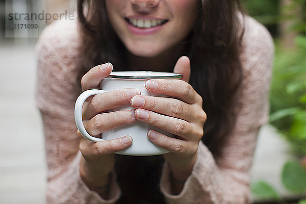Nahaufnahme einer jungen Frau  die im Garten sitzt und Kaffee trinkt