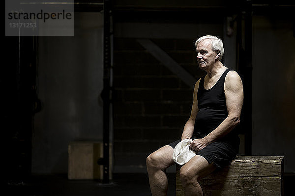 Älterer Mann sitzt ausruhend in dunkler Turnhalle