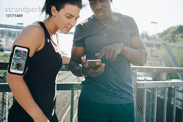 Sportler zeigt einer Sportlerin ein Mobiltelefon  während er am Geländer auf der Brücke steht