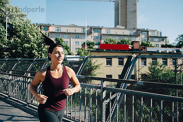 Selbstbewusste Sportlerin joggt auf einer Brücke in der Stadt