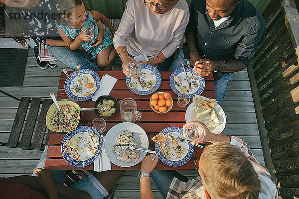 Hochwinkelaufnahme einer Mehrgenerationen-Familie beim Mittagessen am Tisch auf der Veranda