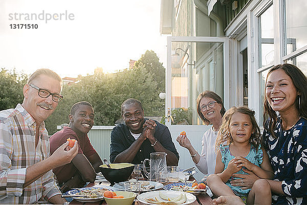 Porträt einer lächelnden Mehrgenerationen-Familie beim Mittagessen bei Tisch auf der Veranda
