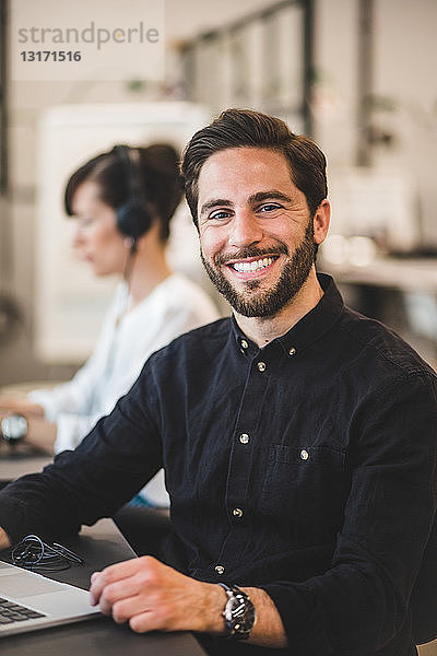Porträt eines lächelnden Geschäftsmannes  der am Schreibtisch im Kreativbüro sitzt
