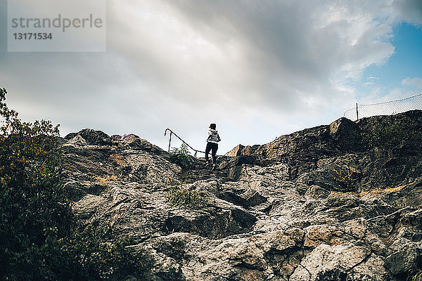 Niedrigwinkelansicht einer Athletin  die auf einem Hügel auf Felsen klettert  gegen den Himmel
