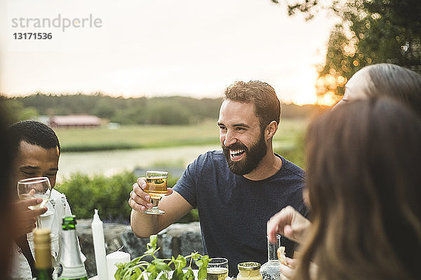 Fröhliche männliche und weibliche Freunde genießen bei Sonnenuntergang ein Drink-Dinner im Hinterhof