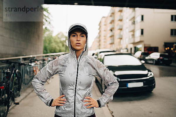 Porträt einer selbstbewussten Sportlerin in nasser Kapuzenjacke auf dem Bürgersteig in der Stadt stehend