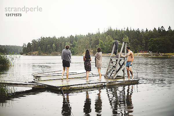 In Handtücher gewickelte Freunde stehen auf einem Steg über dem See vor klarem Himmel