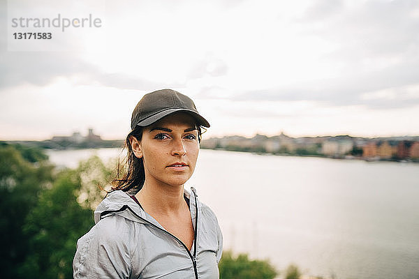 Porträt einer selbstbewussten Sportlerin  die auf einem Hügel am Meer gegen den Himmel steht