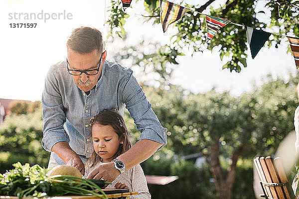 Großvater lehrt Enkelin  Gemüse bei Tisch im Hinterhof zu schneiden