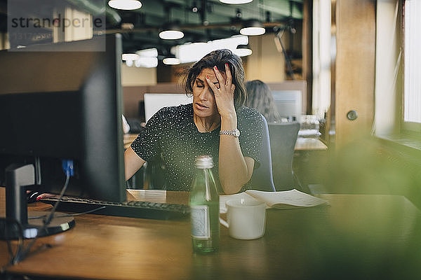 Müde Geschäftsfrau mit dem Kopf in der Hand am Computerschreibtisch im Büro sitzend