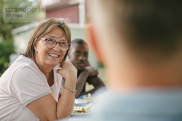 Lächelnde ältere Frau schaut weg  während sie während der Gartenparty am Tisch sitzt