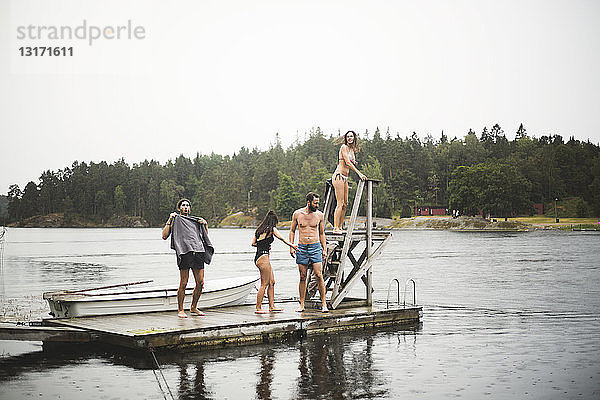 Männliche und weibliche Freunde stehen auf dem Steg über dem See vor klarem Himmel während eines Wochenendausflugs