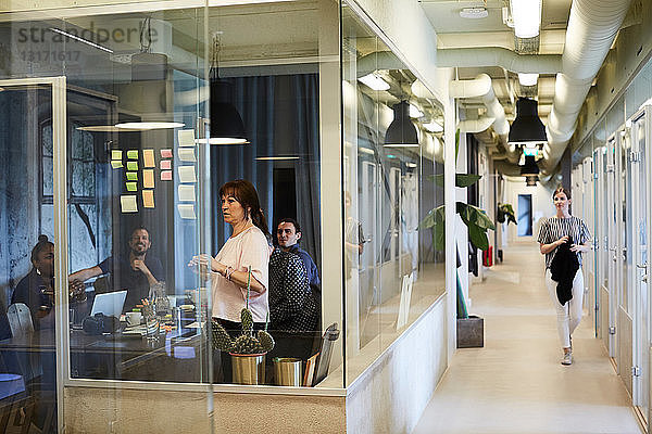 Geschäftsleute beim Brainstorming von Ideen im Sitzungssaal  während eine Kollegin im Korridor geht