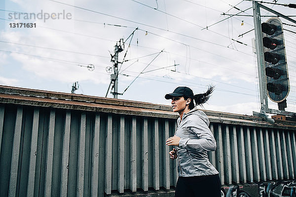 Junge Sportlerin joggt am Zaun auf einer Fußgängerbrücke in der Stadt