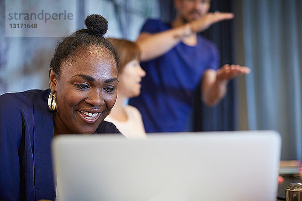 Kreative Geschäftsfrau lächelt  während sie bei einer Besprechung mit Kollegen im Büro den Laptop benutzt
