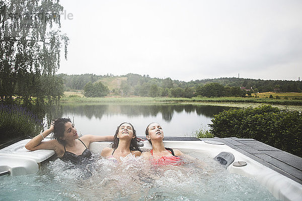 Freundinnen  die sich während eines Wochenendausflugs mit geschlossenen Augen im Whirlpool am See vergnügen