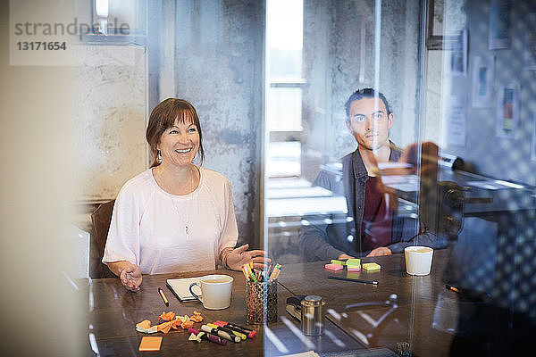 Kreative Geschäftsleute sitzen im Sitzungssaal durch Glas gesehen