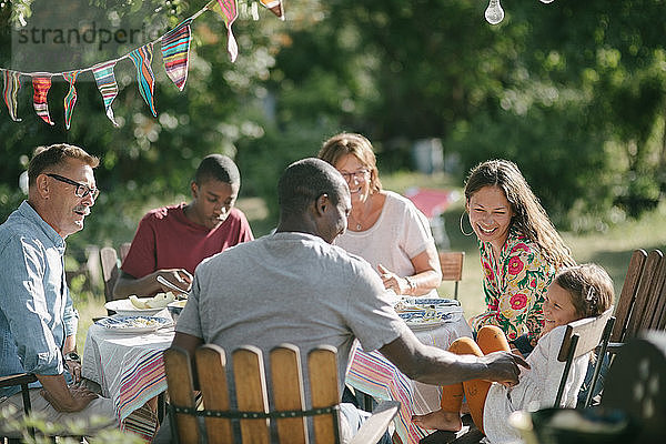 Glückliche Mehrgenerationen-Familie beim gemeinsamen Mittagessen im Garten während der Gartenparty