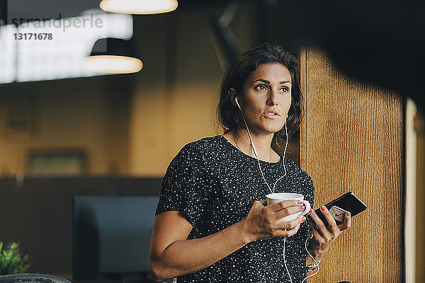Weibliche Führungskraft hält Kaffeetasse während eines Telefongesprächs im Büro mit Kopfhörern