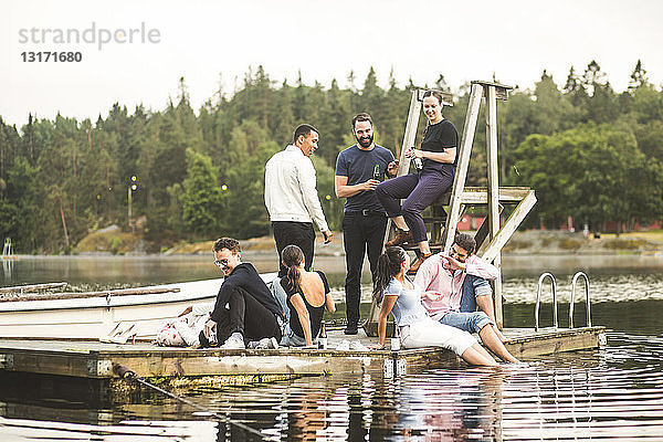 Glückliche männliche und weibliche Freunde genießen am Wochenende auf dem Steg über dem See
