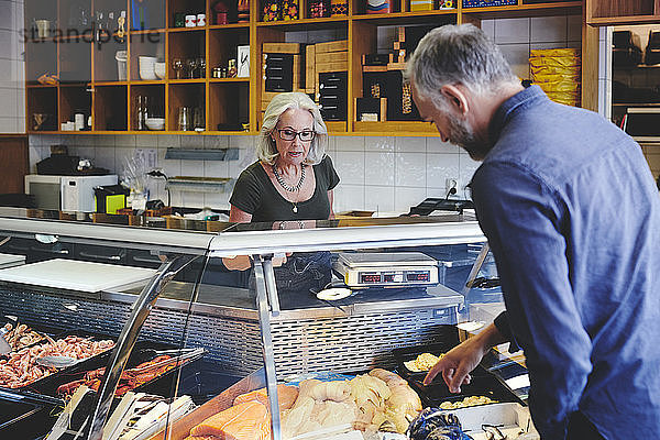 Kunde zeigt einer Verkäuferin im Feinkostladen Meeresfrüchte im Einzelhandel