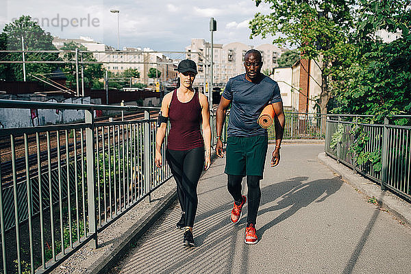 Multi-ethnische männliche und weibliche Athleten unterhalten sich beim Gehen auf einer Fußgängerbrücke in der Stadt