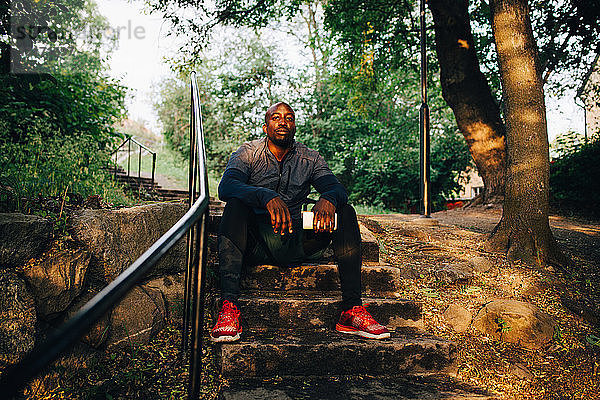 Porträt eines selbstbewussten männlichen Athleten  der auf Stufen im Park sitzt