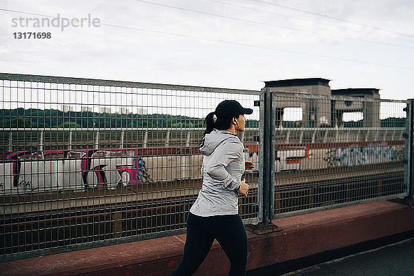 Junge Sportlerin beim Joggen am Zaun auf einer Brücke in der Stadt