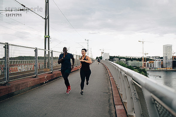 Männliche und weibliche Athleten laufen in voller Länge auf einer Fußgängerbrücke in der Stadt