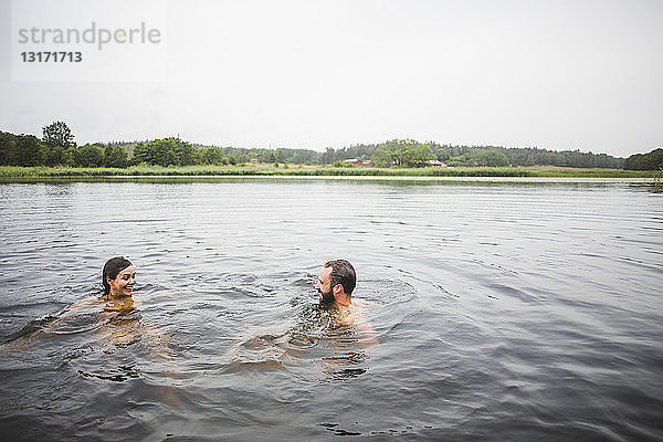 Glückliche männliche und weibliche Freunde schwimmen am Wochenende im See bei klarem Himmel