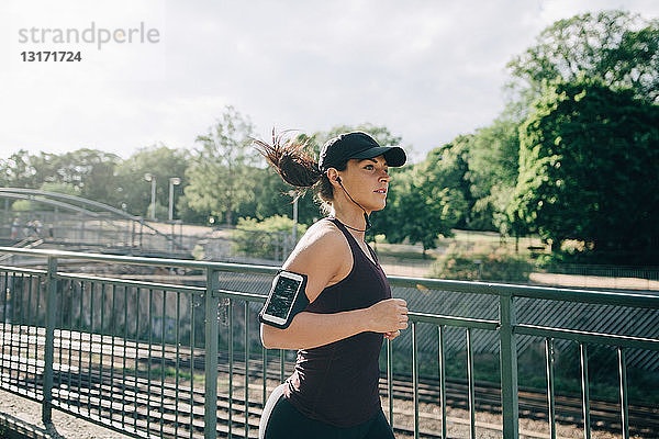 Selbstbewusste Sportlerin  die beim Joggen auf einer Brücke in der Stadt über In-Ear-Kopfhörer Musik hört