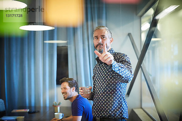 Ein reifer Geschäftsmann  der während einer Besprechung im Büro auf einen auf Glas geklebten Zettel zeigt