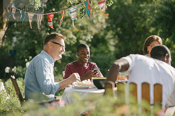 Glückliche Mehrgenerationen-Familie beim gemeinsamen Mittagessen im Garten während der Gartenparty