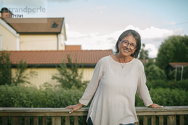 Porträt einer älteren Frau  die vor dem Geländer der Veranda steht