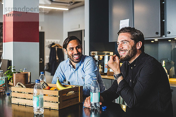 Männliche Kollegen lächeln  während sie im Büro am Tisch sitzen