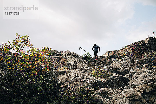 Niedrigwinkelansicht eines männlichen Athleten beim Klettern an Felsen auf einem Hügel gegen den Himmel