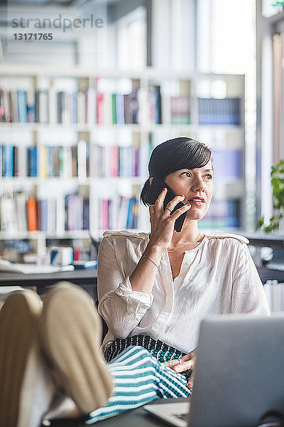 Kreative Geschäftsfrau  die am Schreibtisch im Büro entspannt mit dem Handy telefoniert