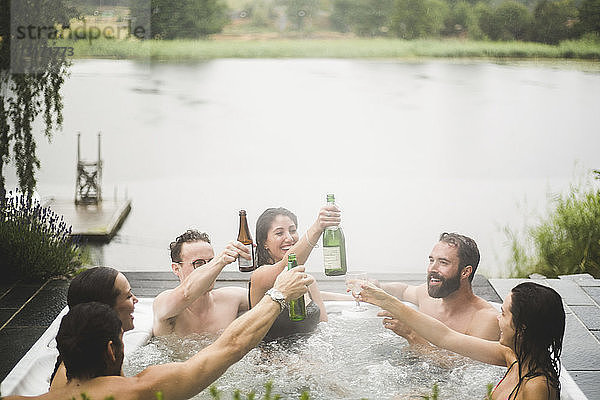 Sorglose männliche und weibliche Freunde  die während eines Wochenendausflugs im Whirlpool am See Getränke genießen