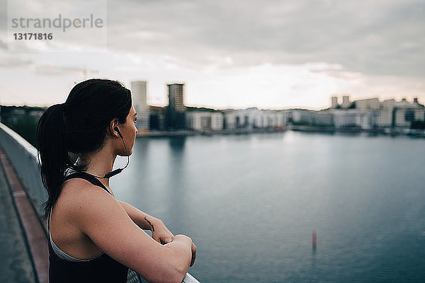 Seitenansicht einer Athletin  die die Stadt betrachtet  während sie auf einer Fußgängerbrücke über das Meer steht