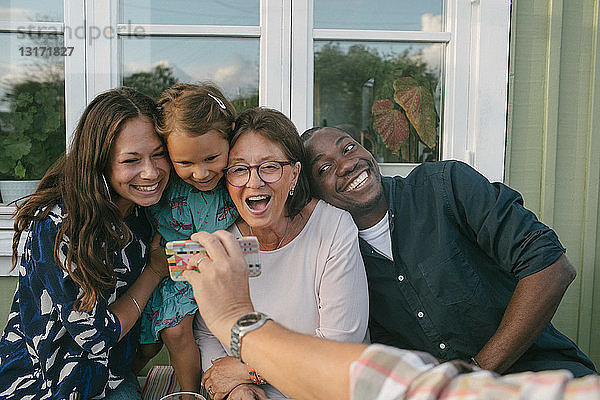 Ausgeschnittenes Bild eines Mannes  der auf der Veranda ein Mobiltelefon einer fröhlichen Familie zeigt