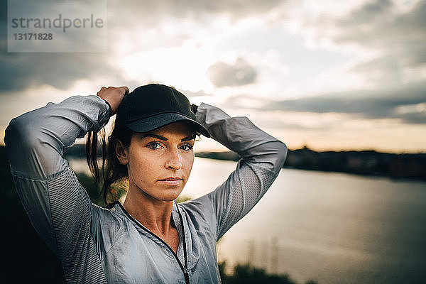 Porträt einer selbstbewussten Sportlerin  die sich bei Sonnenuntergang die Haare bindet  während sie auf einem Hügel steht