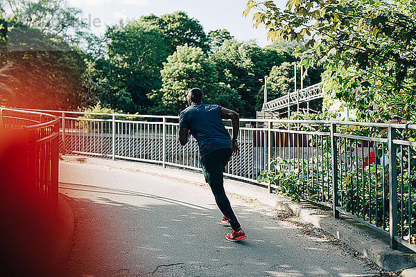Rückansicht eines Sportlers  der auf einer Fußgängerbrücke in der Stadt joggt