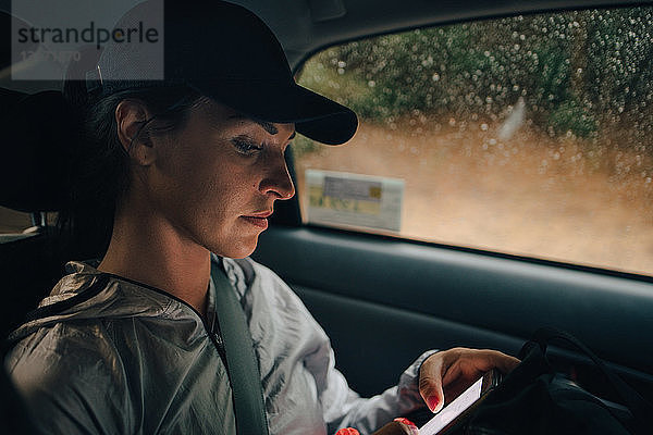 Sportlerin  die während der Regenzeit im Auto unterwegs ist und ein Mobiltelefon benutzt