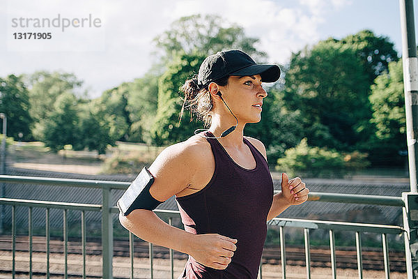 Selbstbewusste Sportlerin hört Musik beim Joggen auf der Brücke in der Stadt