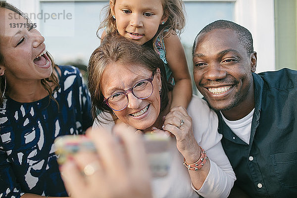 Ausgeschnittenes Bild eines Mannes  der seiner glücklichen Familie auf der Veranda ein Mobiltelefon zeigt