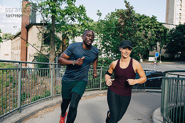 Entschlossene männliche und weibliche Freunde joggen auf der Brücke in der Stadt