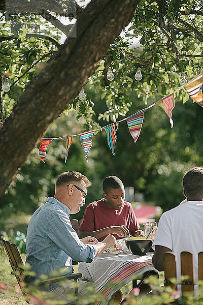 Junge isst während der Gartenparty mit Vater und Großvater auf der Terrasse zu Mittag